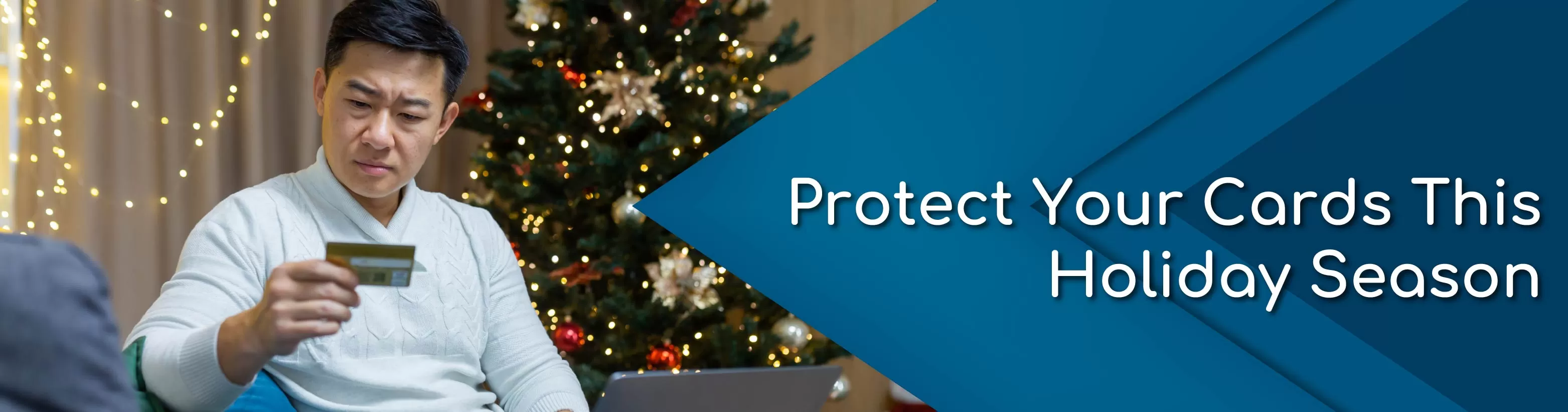 Man looking at card while on laptop sitting on couch next to Christmas tree